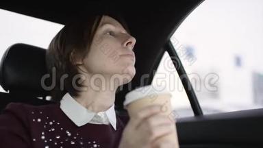 穿着白色上衣和栗色毛衣的棕色头发的漂亮女人在车里堵车，喝咖啡
